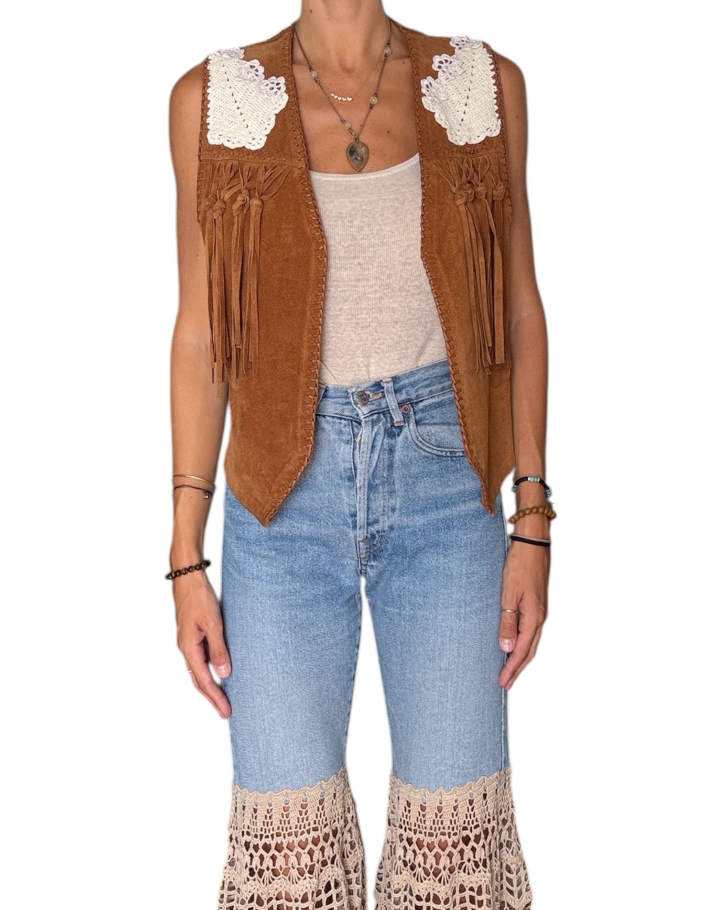 Person wearing a brown suede vest with fringe, beige top, and blue jeans on a white background